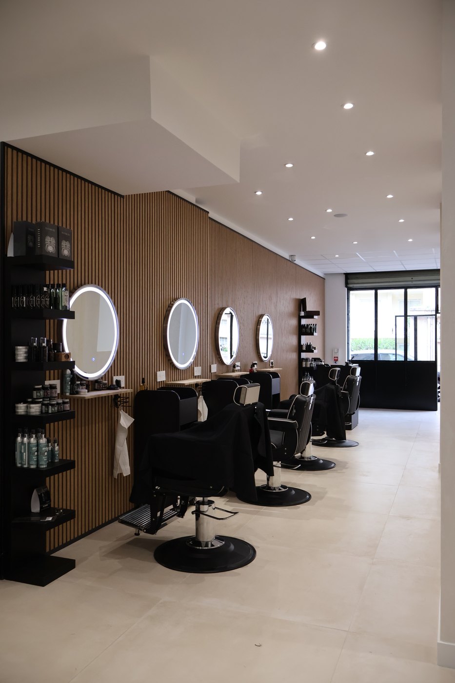 Espace AURA Men — mur en tasseaux de bois, miroirs ronds lumineux et fauteuils barbier
